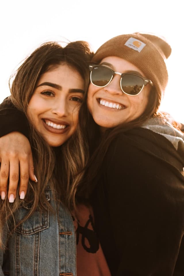 Duas amigas abraçadas, rindo, no fim da tarde