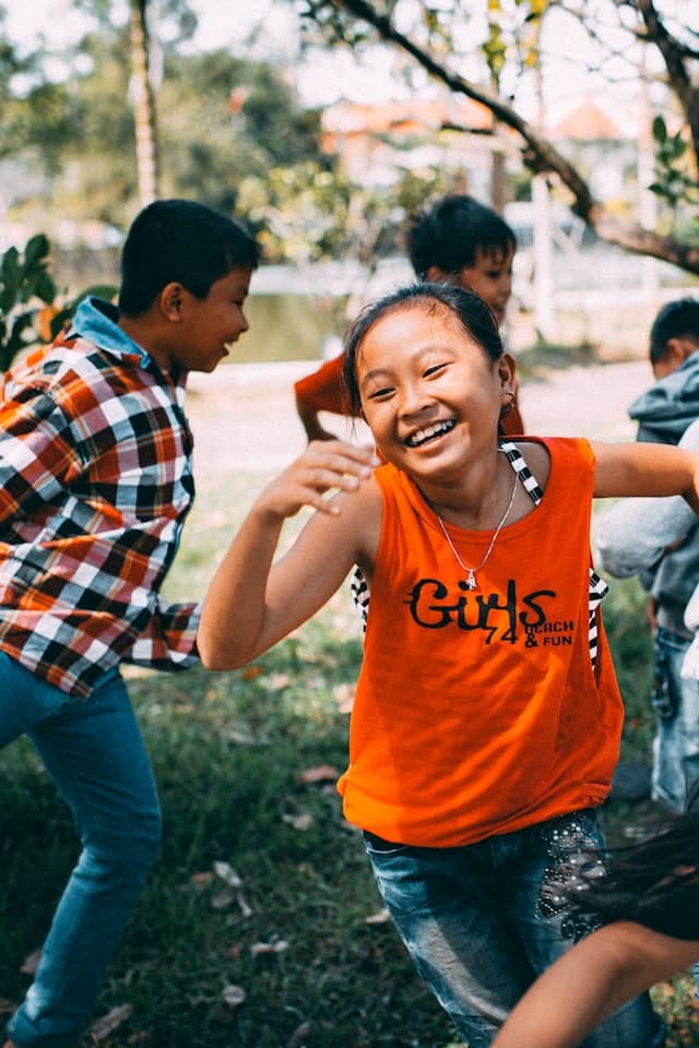 Menina de camiseta laranja rindo entre outras crianças