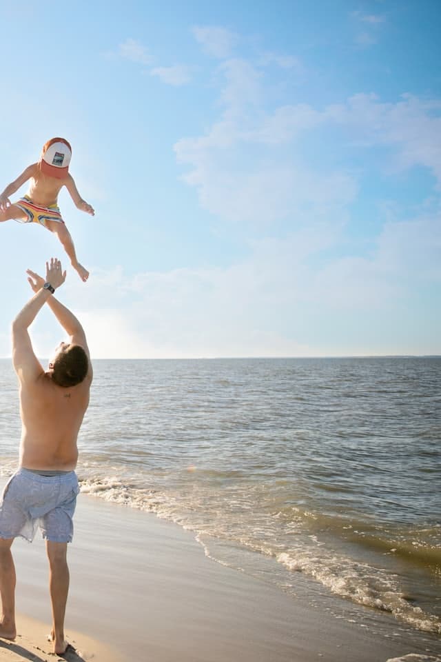 Pai jogando o filho pequeno para o alto na beira da praia